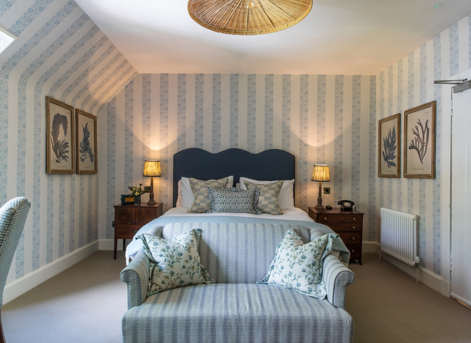 A cozy bedroom in the Cottage Room at the Cromlix Hotel in Dunblane, featuring a blue sofa and striped wallpaper.